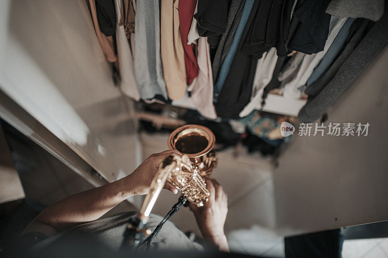 top view of asian chinese mid adult man practicing saxophone facing his wardrobe as soundproof to reduce the sounds disturbing his neighbor  in his apartment